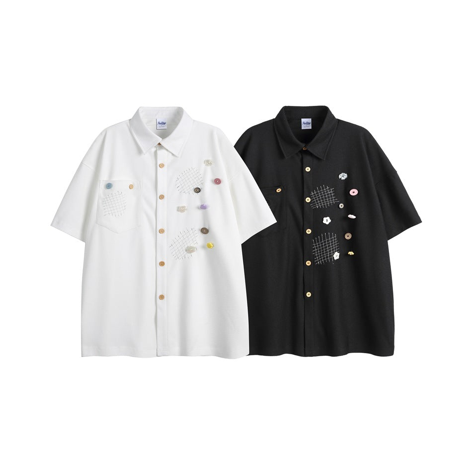 White and black short-sleeve button-up shirts displayed side by side, with chest pockets, grid patches and colorful accents.