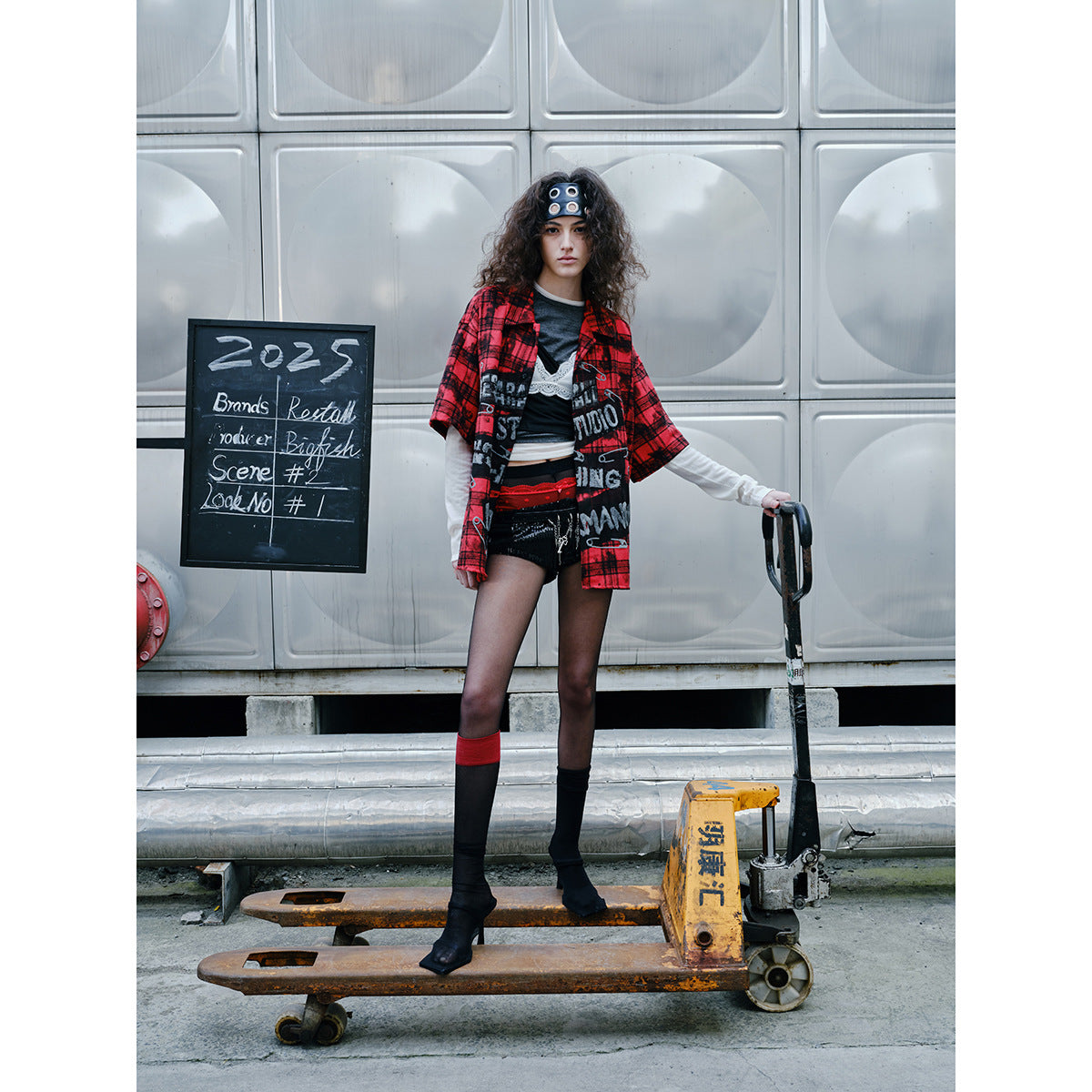Model wearing a red-and-black plaid graphic shirt, layered tops, black shorts, and mismatched knee-high socks.