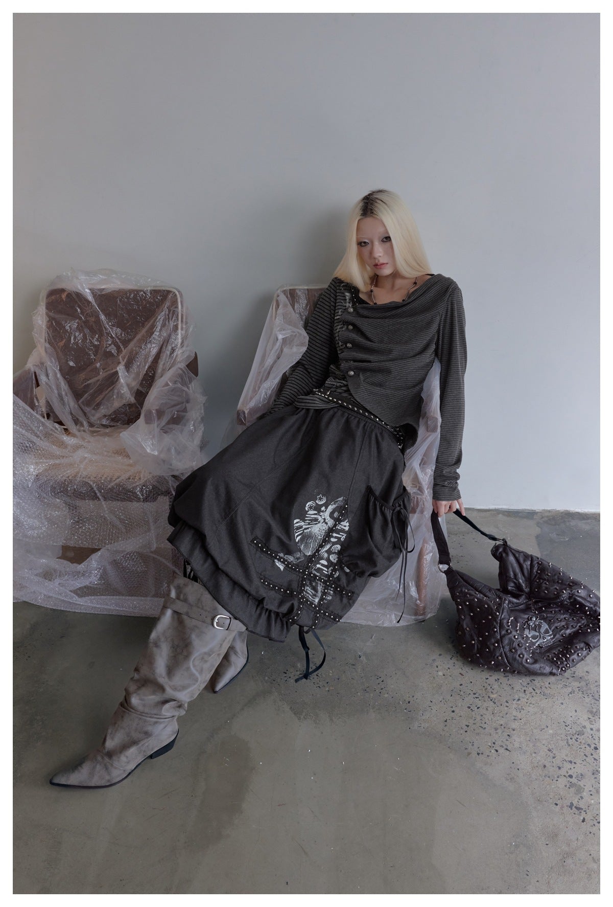 Model in a charcoal striped draped top and graphic black skirt, with pale gray boots and a studded bag.