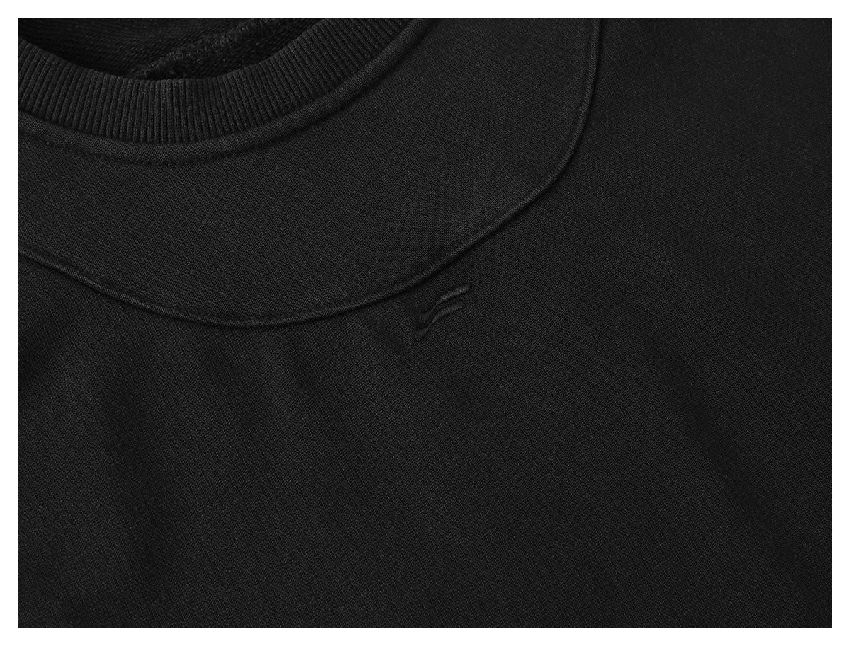 Close-up of a black crew neckline with ribbed collar and a small tone-on-tone embroidered emblem.