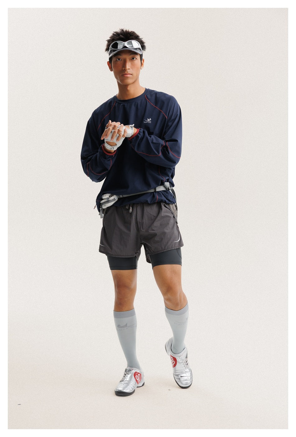Front view of a man wearing a navy long-sleeve top with red seam piping, charcoal running shorts, and light gray knee socks.