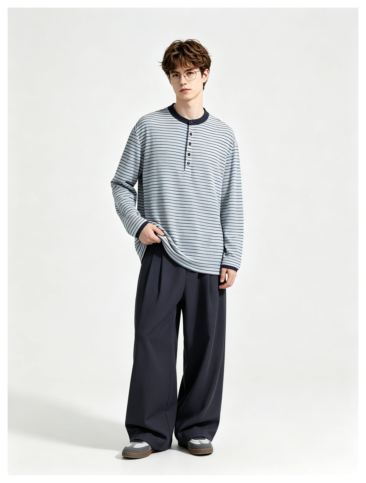 Model facing forward in a blue striped long-sleeve Henley top with navy trim, wide navy trousers and sneakers