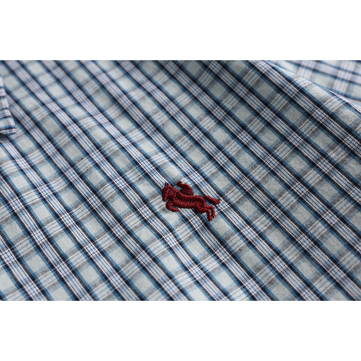 Close-up of a red embroidered animal logo on blue, gray, and white plaid fabric.