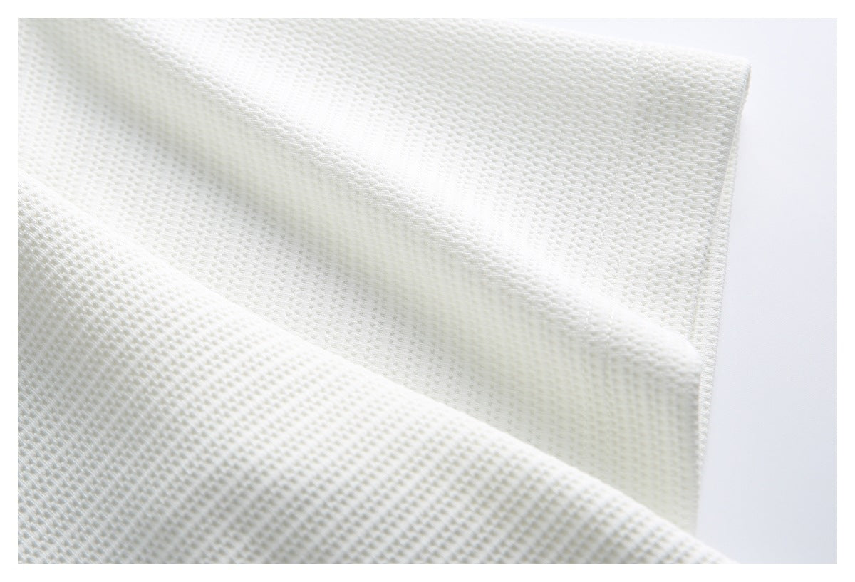 Close-up of white knit fabric draped to show its textured stitch pattern.