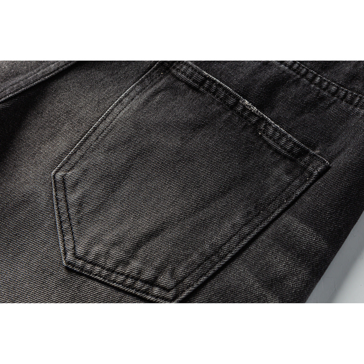 Close-up of a stitched rear patch pocket on black washed denim shorts.