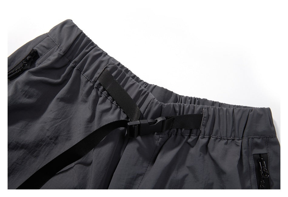 Close-up of charcoal shorts showing the elastic waistband, black buckle belt, and zip pocket openings.