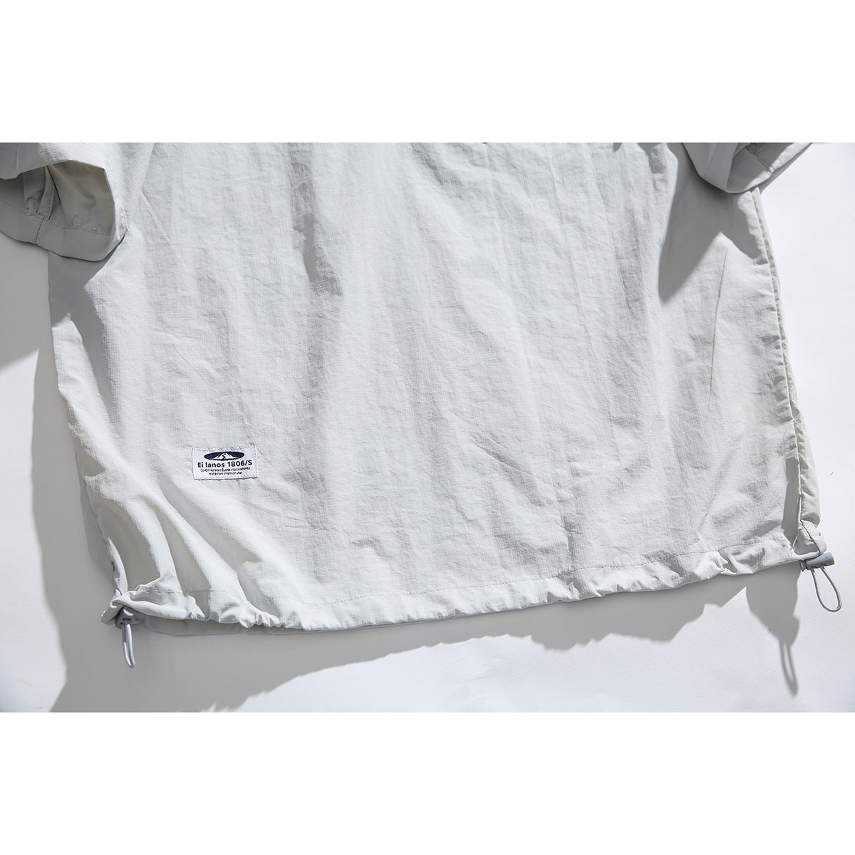 Close-up of the pale gray pullover shirt's lower hem, gathered drawcords and small sewn label.
