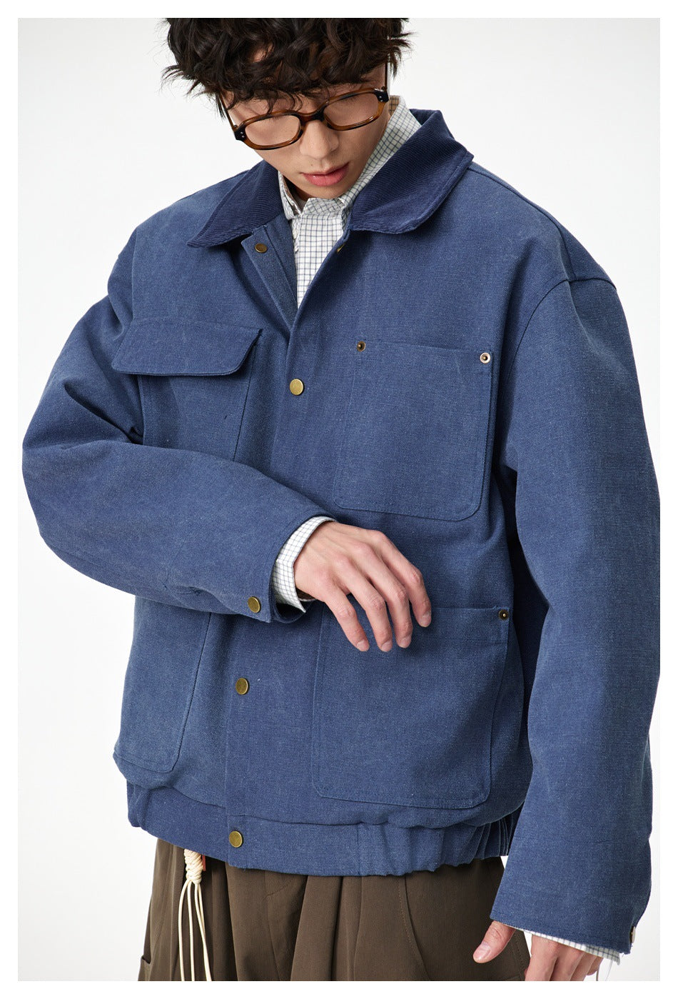 Close view of a model wearing a blue utility jacket with a wide collar, brass-tone snaps and multiple pockets.