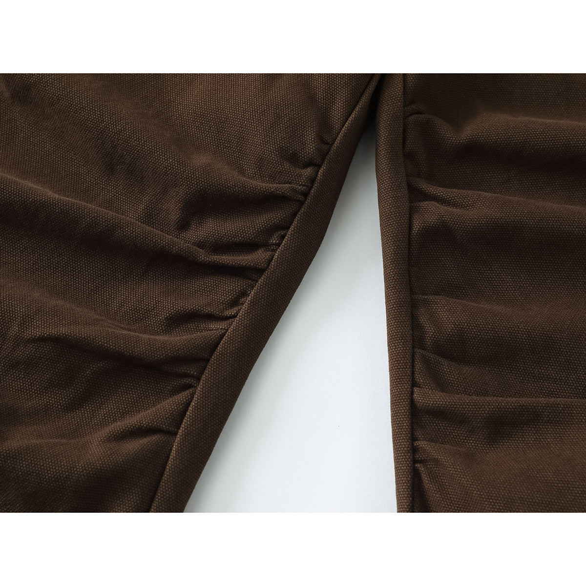 Close-up of dark brown trousers showing textured fabric and overlapping seams.