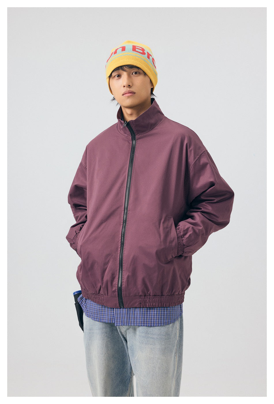 Front view of a model wearing a zipped plum jacket with elastic cuffs and hem, over a blue checked shirt.