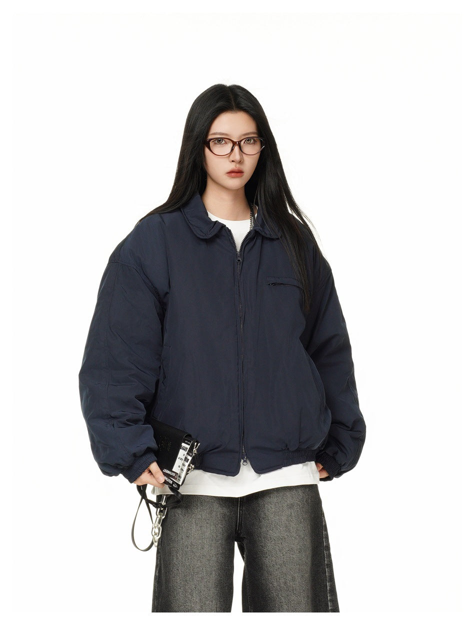 Model wearing a navy zip-up jacket with collar over a white tee and gray jeans, holding a black wallet