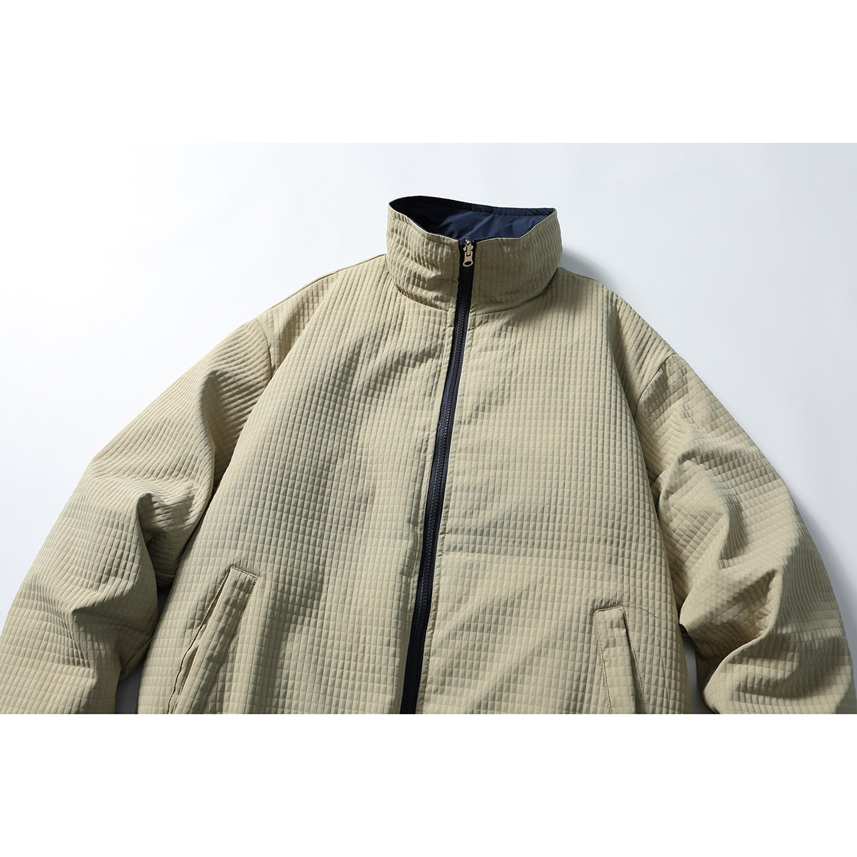 Front view of a light khaki quilted jacket with a high collar, navy zipper, and slanted pockets.