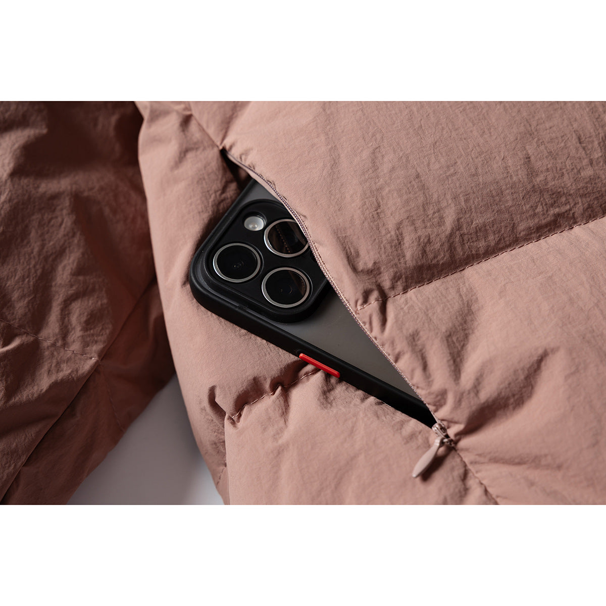 A phone sits in a zippered pocket on the dusty rose jacket, shown in close-up.