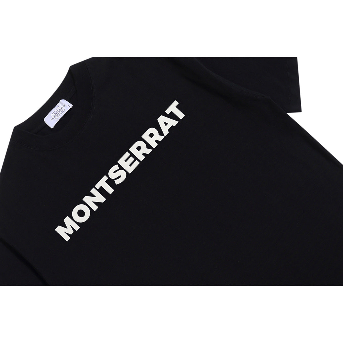 Close-up of a black T-shirt showing white MONT SERRAT lettering across the chest and the neck label.