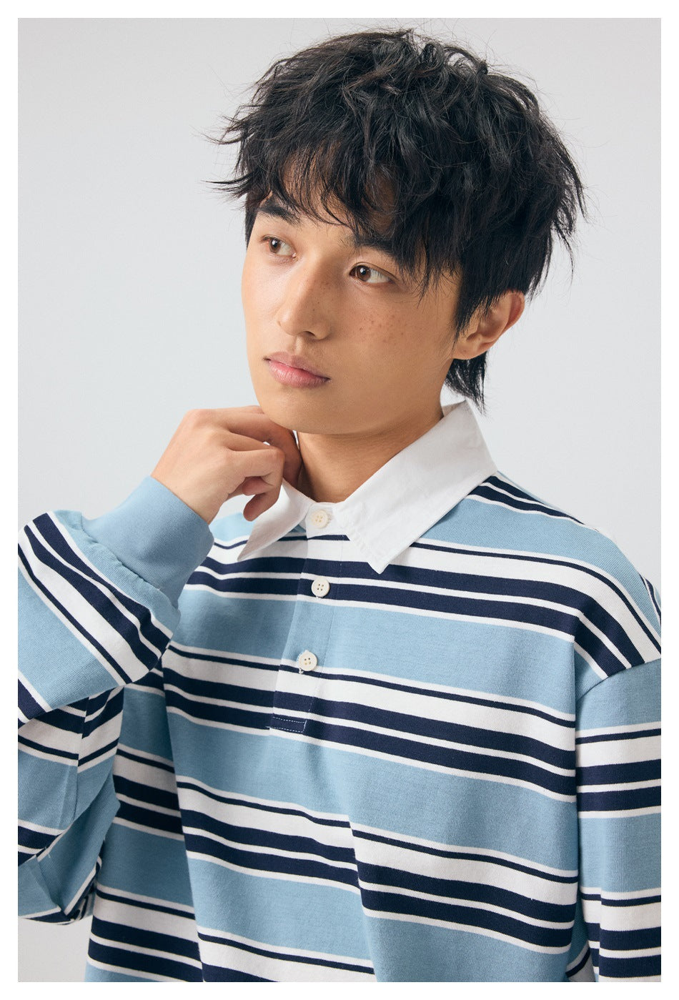 Close-up of a model wearing a light blue, navy and white striped rugby shirt with a white collar and button placket.
