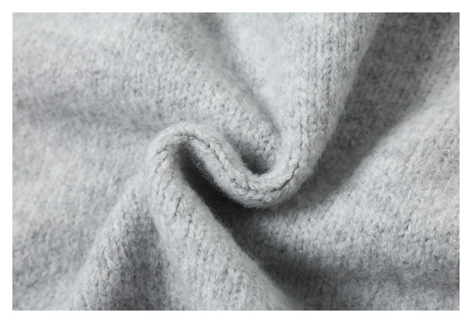 Close-up of light gray knitted fabric gathered into a curled fold, showing its stitch texture.