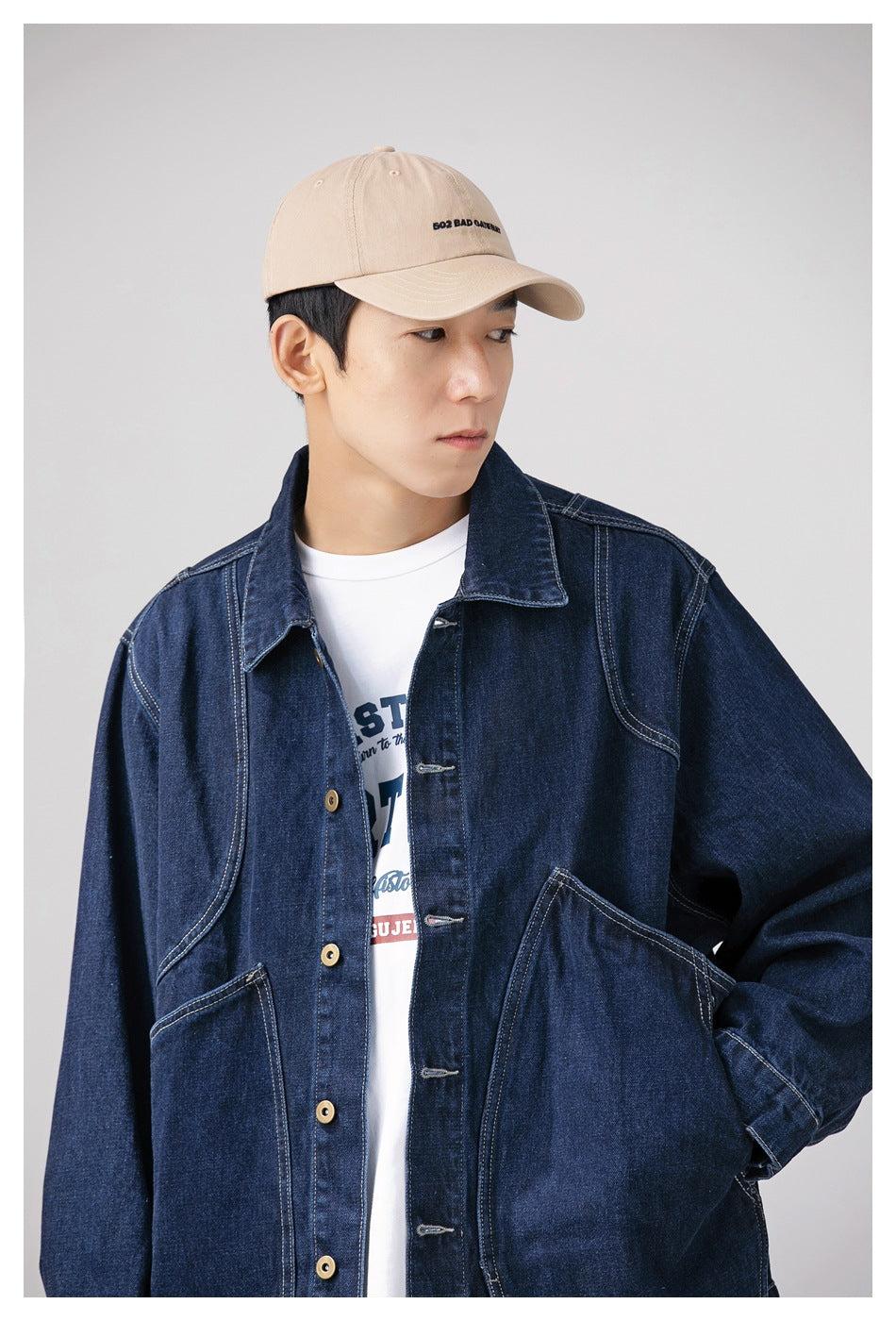 Close view of a model wearing a dark indigo denim jacket with contrasting stitching and a beige cap.