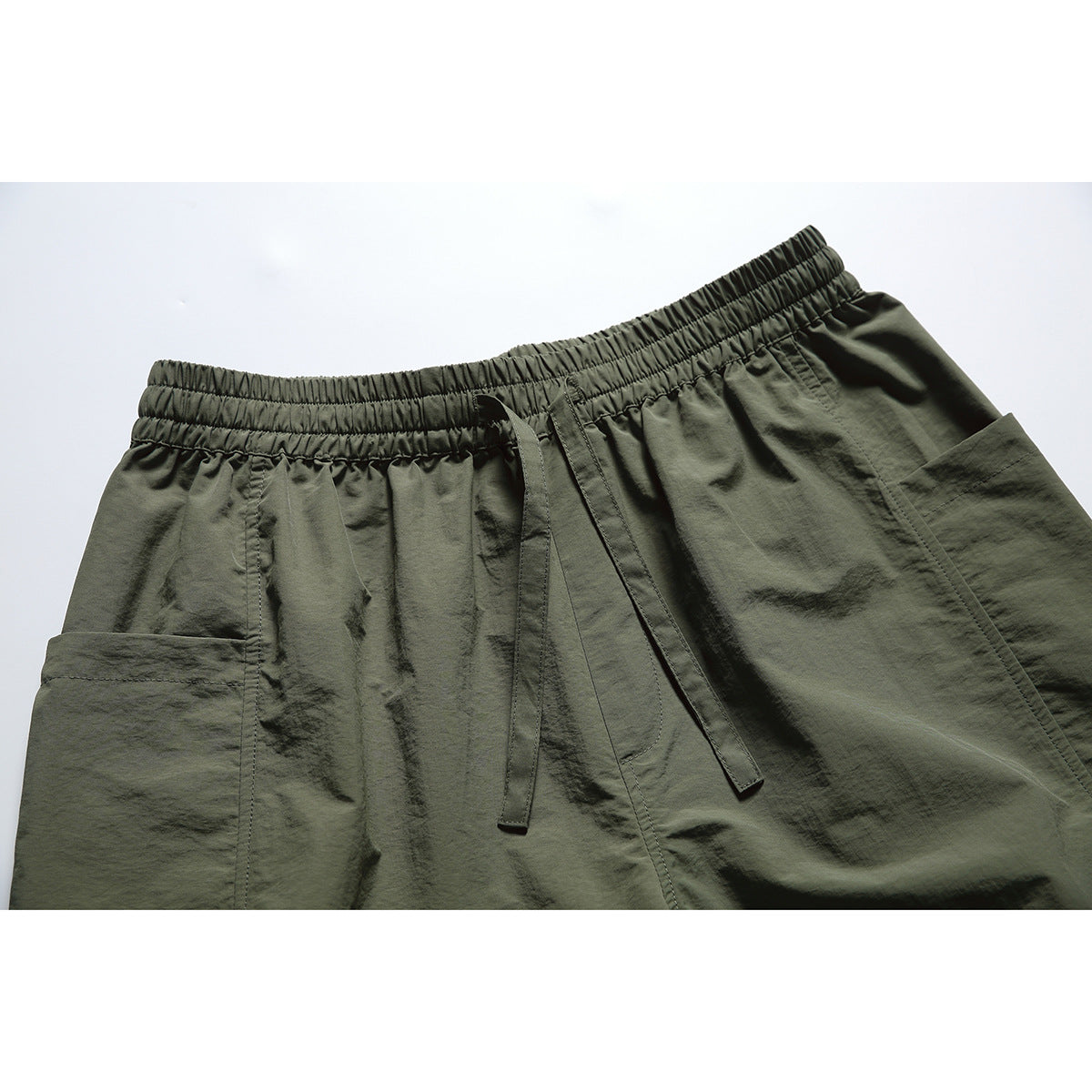 Close-up of olive shorts showing the gathered elastic waistband, drawstring and large side pocket.