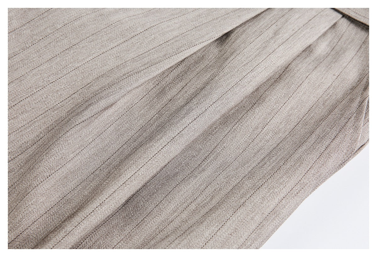 Close-up of taupe-gray herringbone trouser fabric with stitched pleats and folded panels.