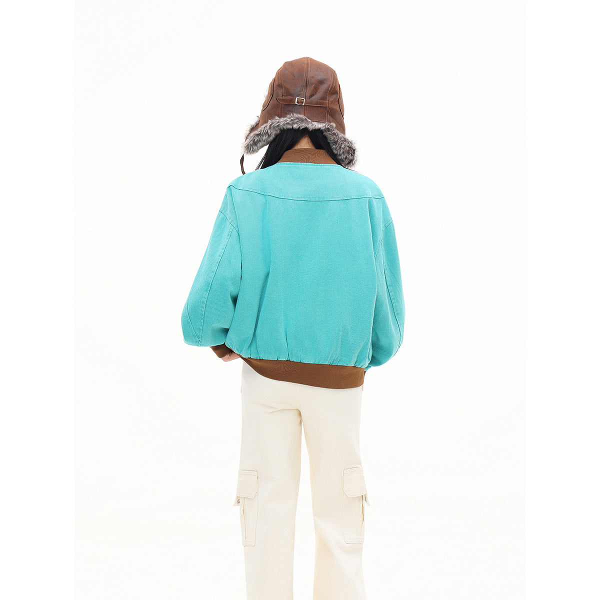 Back view of a model wearing a turquoise bomber jacket with a brown ribbed hem and cream cargo pants.