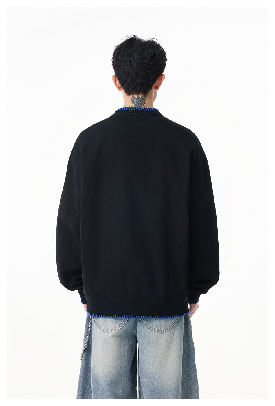 Rear view of a model wearing a black oversized pullover with blue stitching at the collar, cuffs and hem.