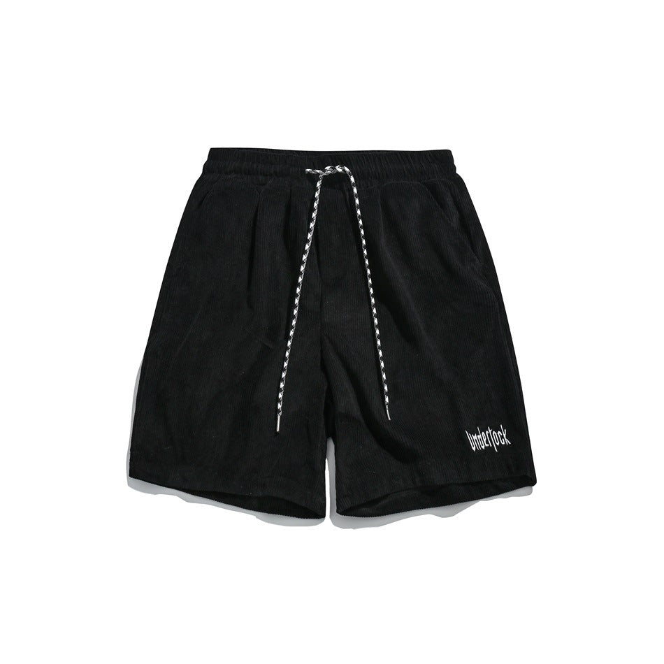 Black corduroy-style shorts with elastic waist, patterned drawstring and small white embroidered text, flat lay