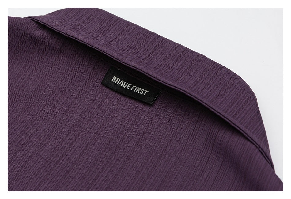 Close-up of a dark plum ribbed garment collar with a sewn-in BRAVE FIRST label.
