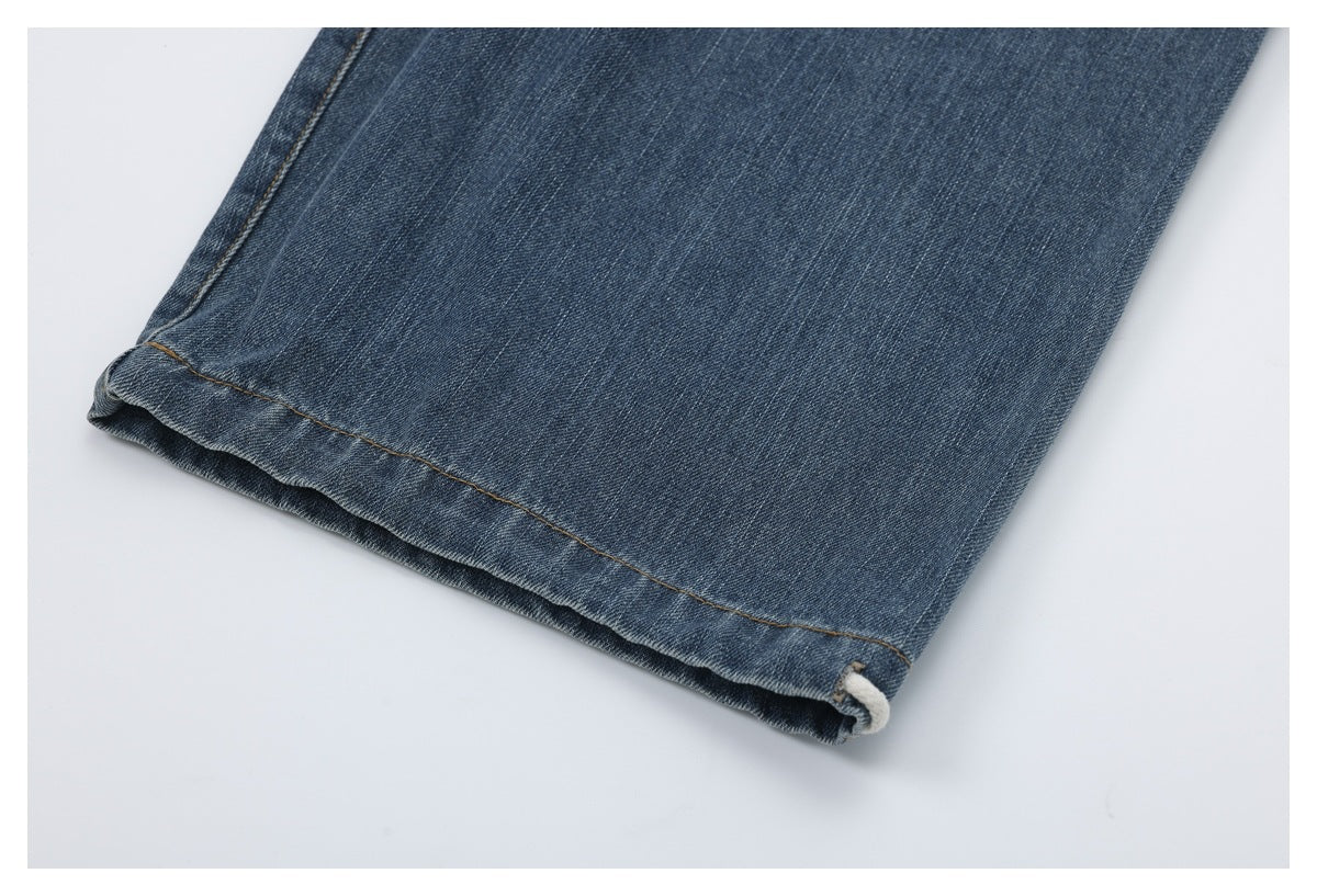 Close-up of the blue denim pant hem with tan stitching and a cream cord loop.