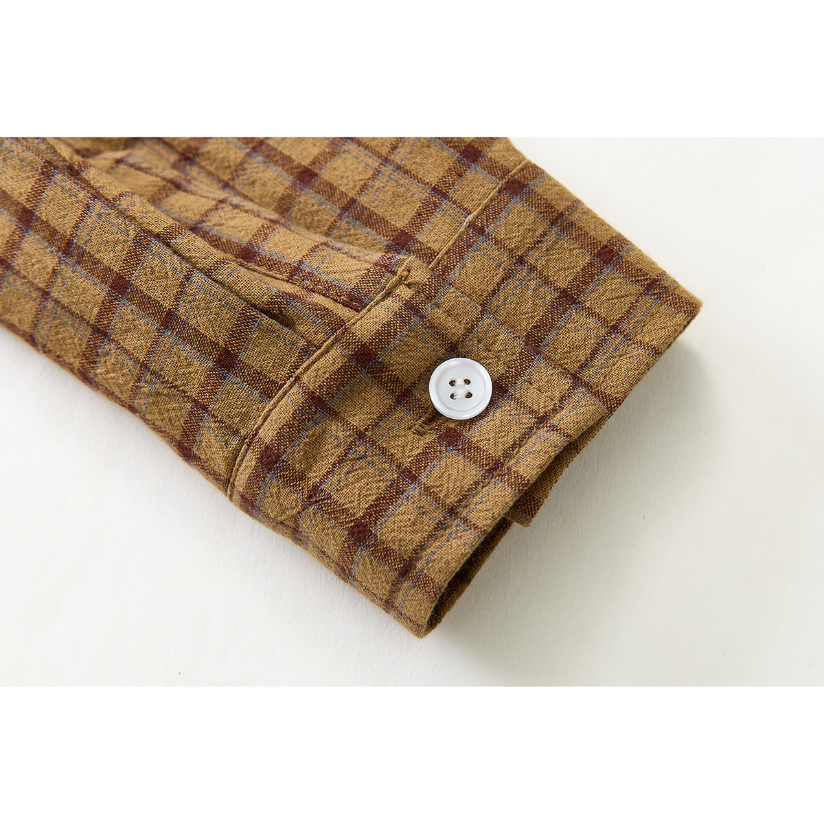 Close-up of a brown plaid shirt cuff with a white button and visible stitching.