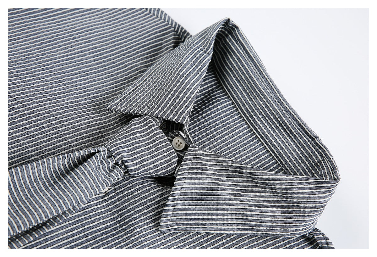 Close-up of a pointed collar and button on a dark shirt with narrow light stripes.