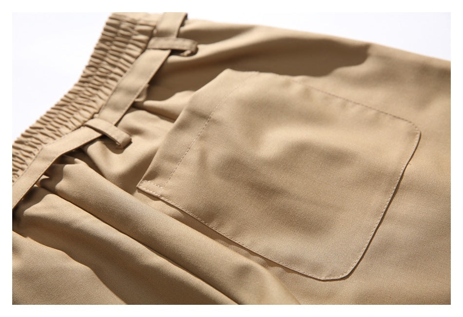Close-up of tan trousers showing the elasticated waistband, belt loops, and large patch pocket.