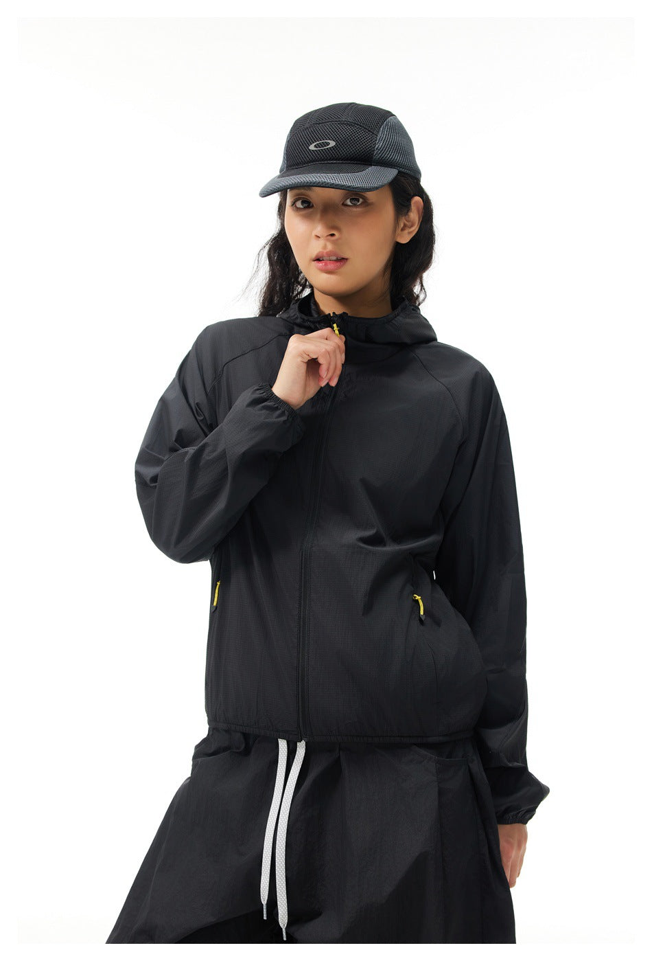 Front view of a model wearing a black hooded jacket with a full zip and yellow pocket pulls.