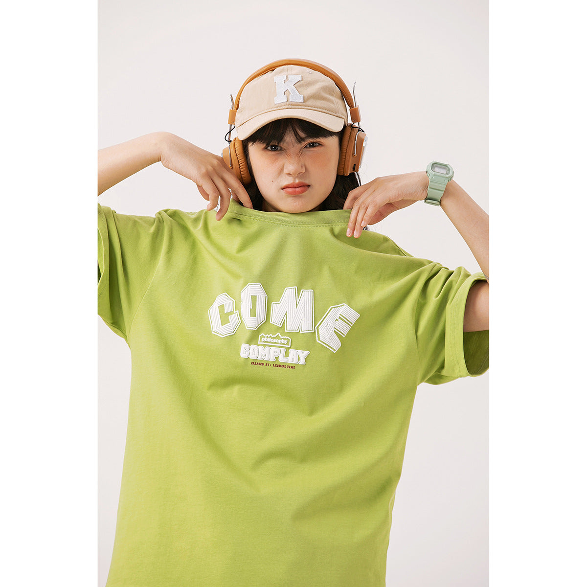 Model holds up an oversized lime-green T-shirt with a large white chest graphic.