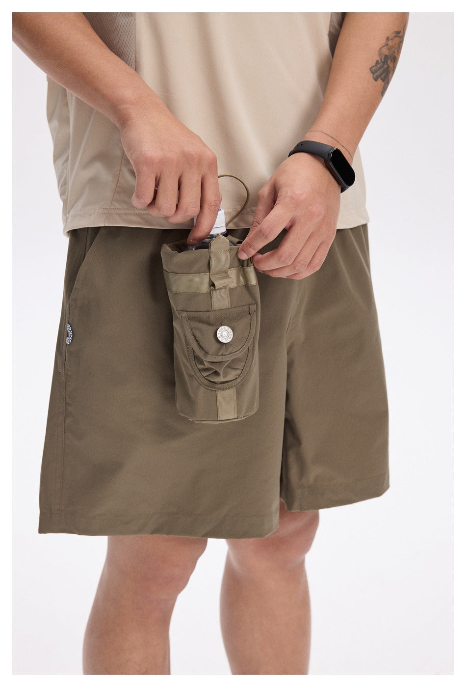 Close-up of khaki shorts with a button-flap utility pouch holding a bottle, worn by a person.