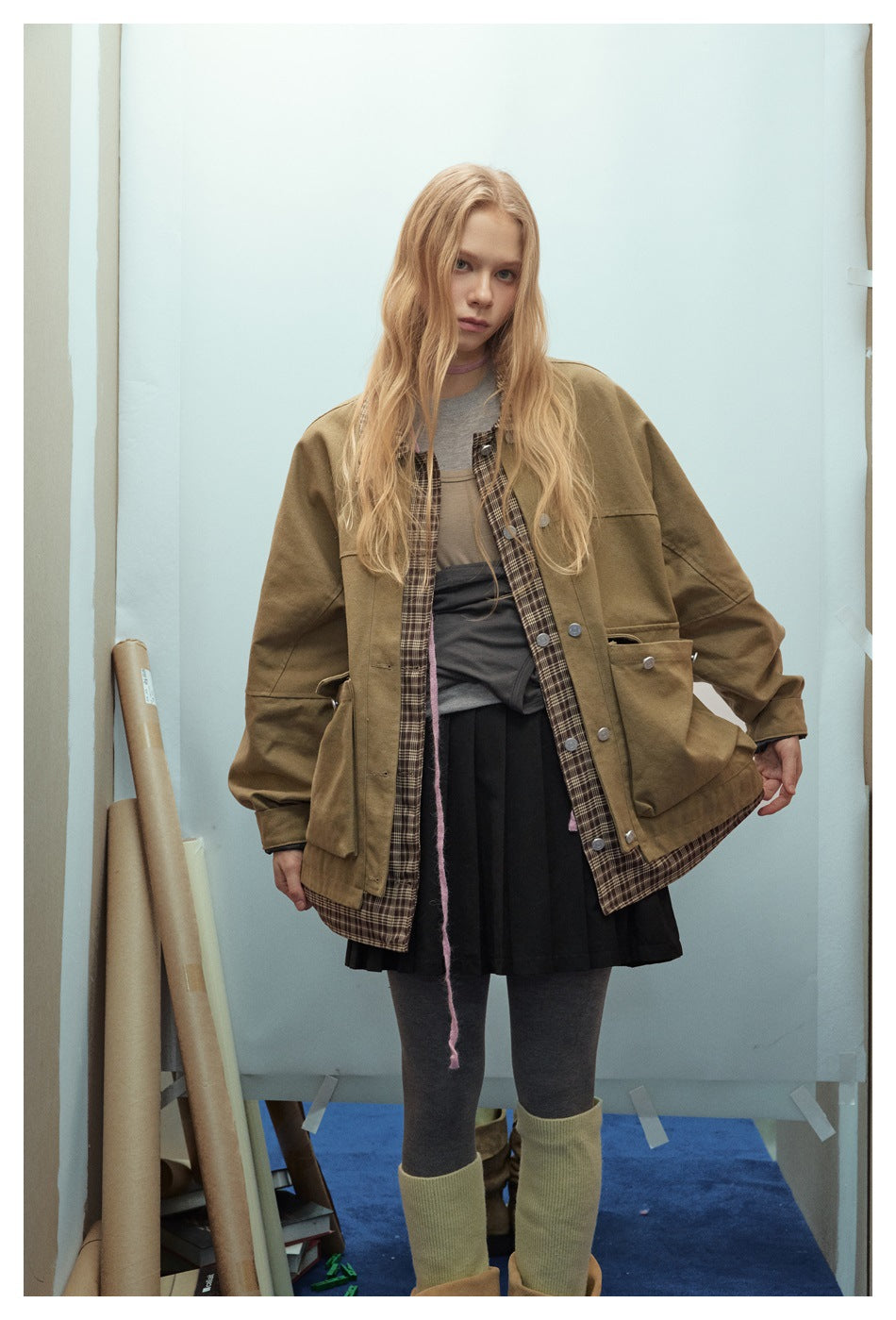 Front view of a model wearing an oversized olive-brown jacket with large pockets and a plaid inner placket and hem.