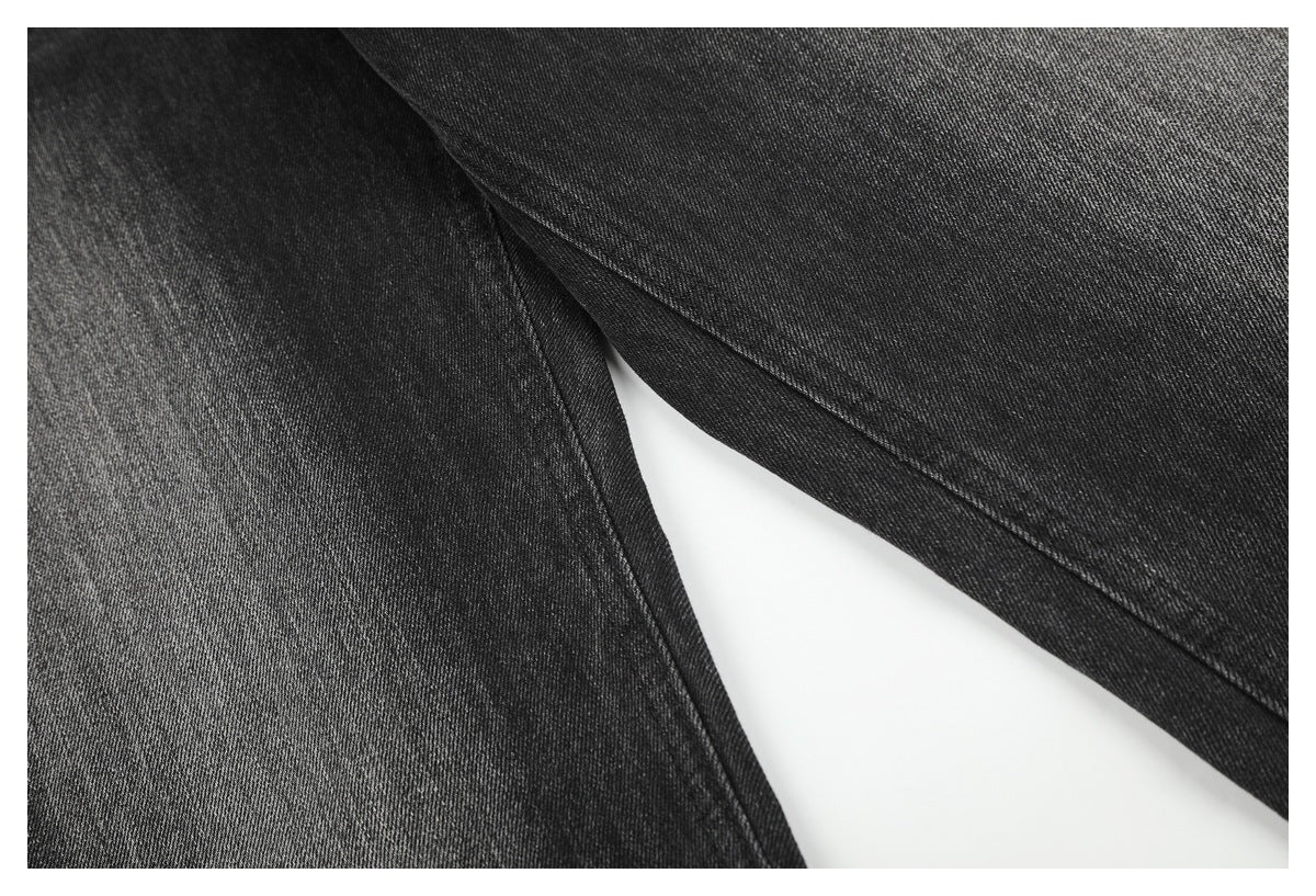 Close-up of charcoal-black denim jeans showing overlapping stitched panels and diagonal twill texture.