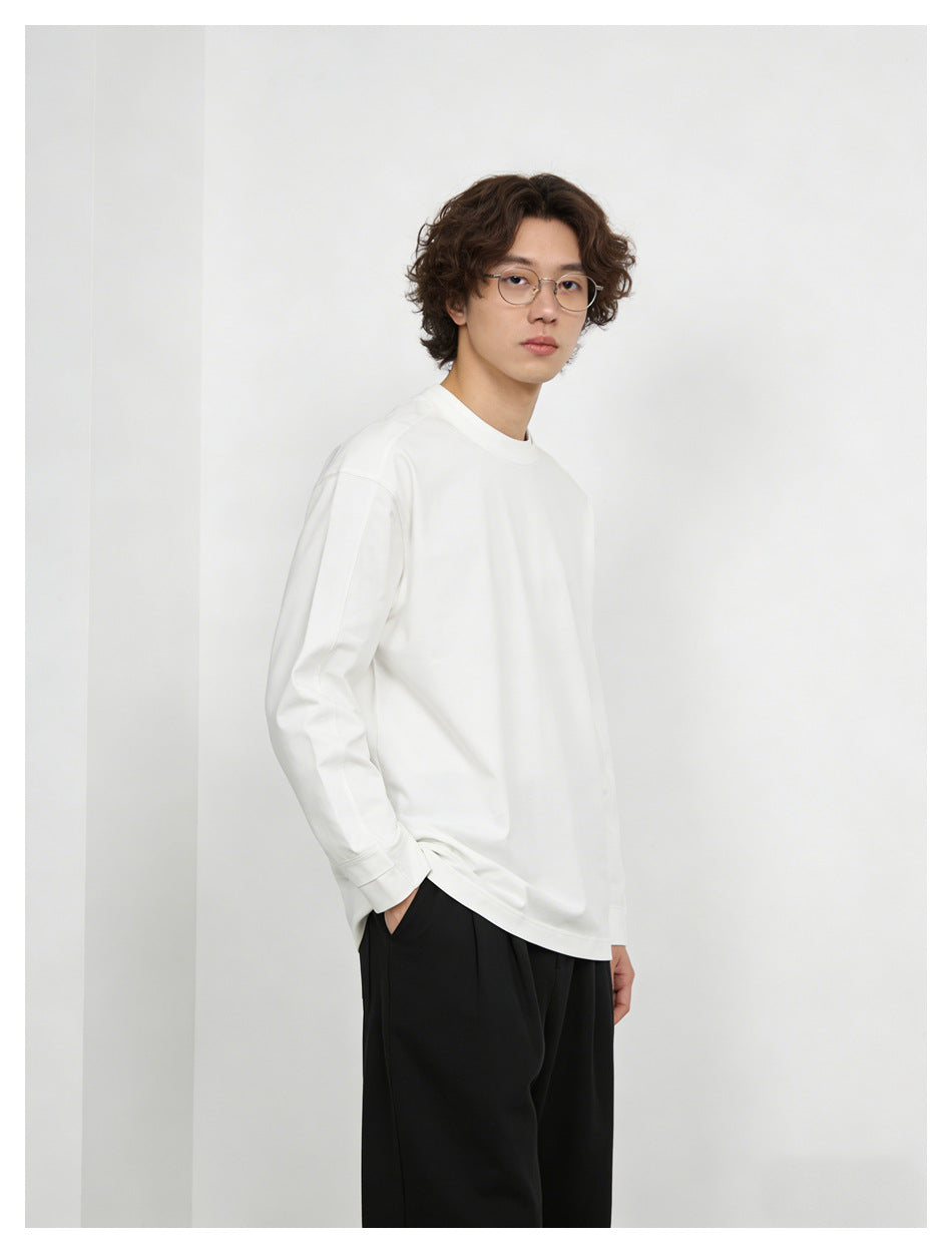 Model wearing a loose white long-sleeve crewneck shirt with black trousers, shown at a three-quarter angle.