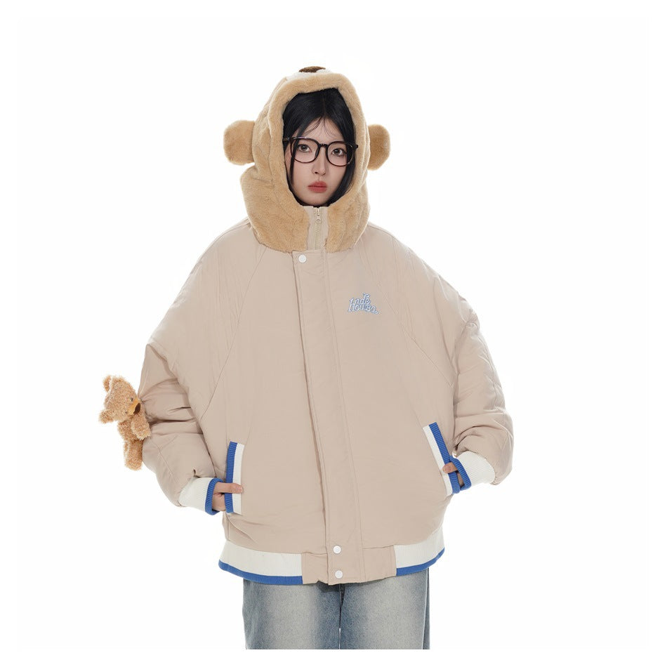 Person wearing a khaki puffer jacket with the bear hood up, striped trim, a sleeve teddy bear and jeans