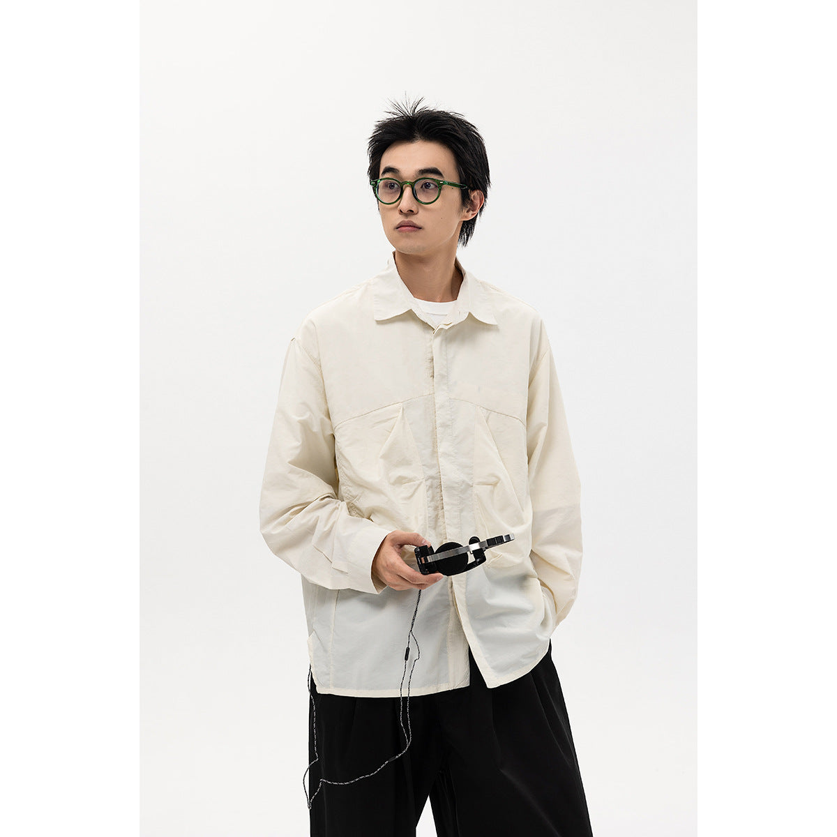 Model wearing an oversized ivory button-up shirt with large front pockets and black trousers.