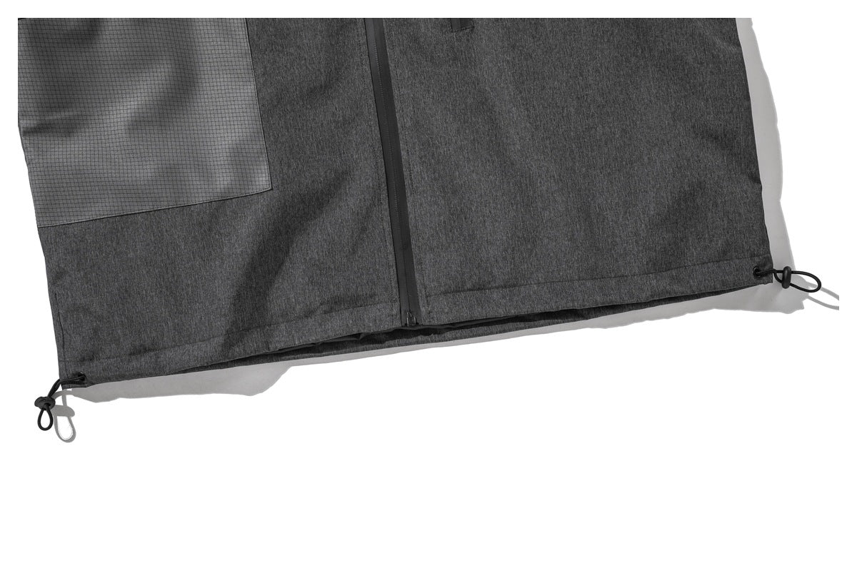 Close-up of the jacket's lower front, showing the zipper, grid-panel pocket and adjustable hem cords.