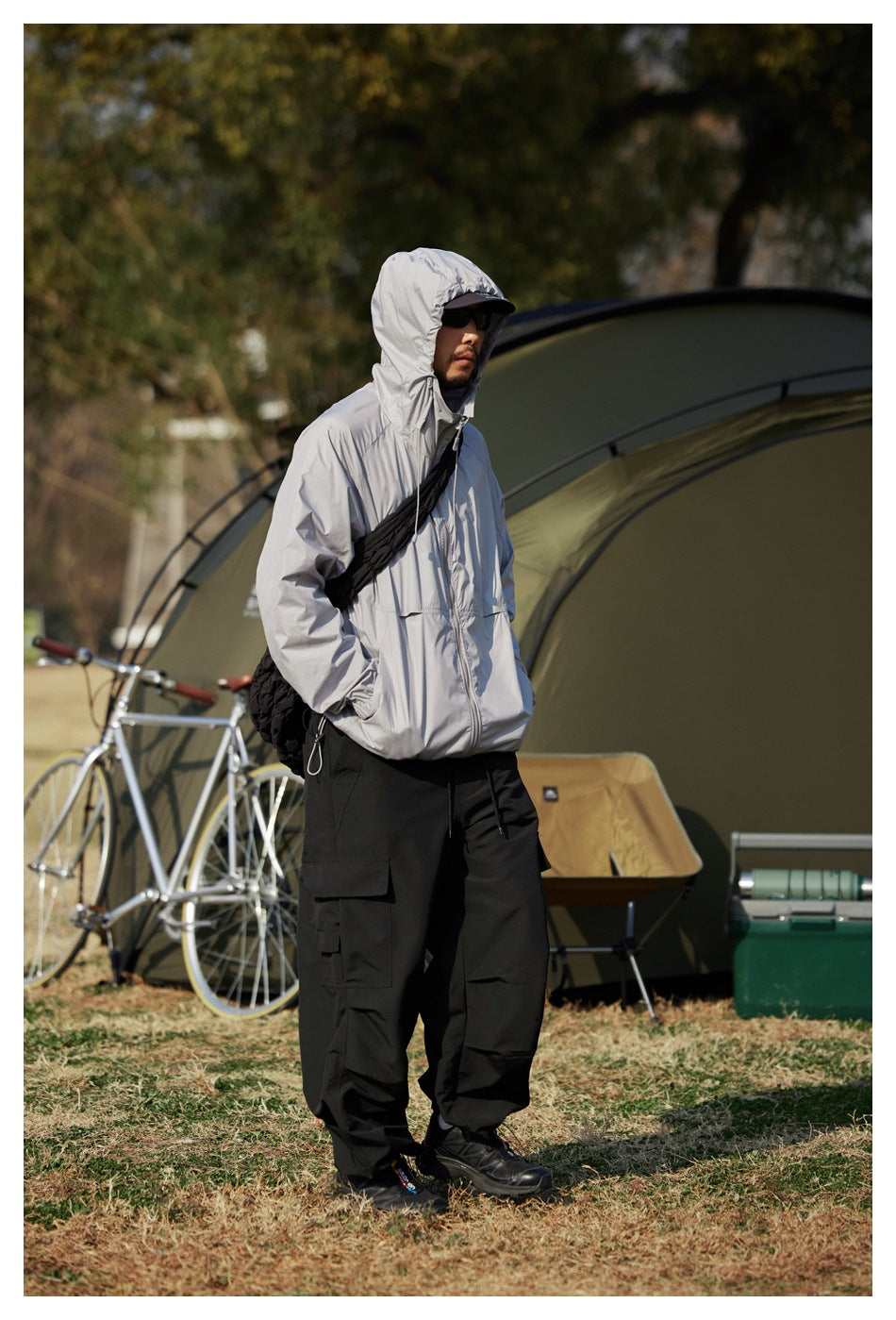 Person wearing the gray hooded zip jacket with hood up and hand in pocket, with black cargo pants outdoors