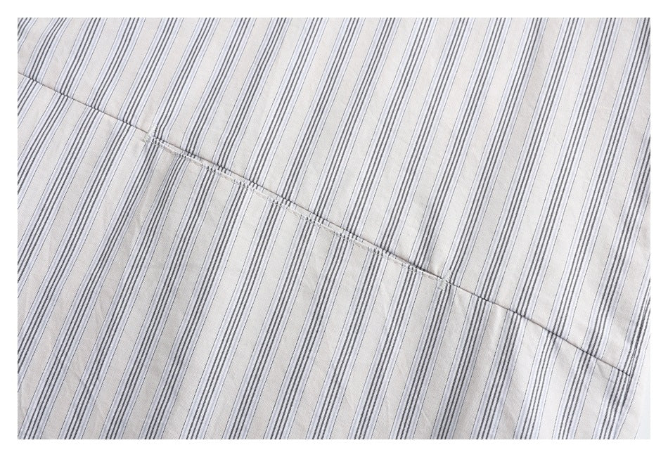 Close-up of a stitched seam across white shirt fabric with fine gray vertical stripes.