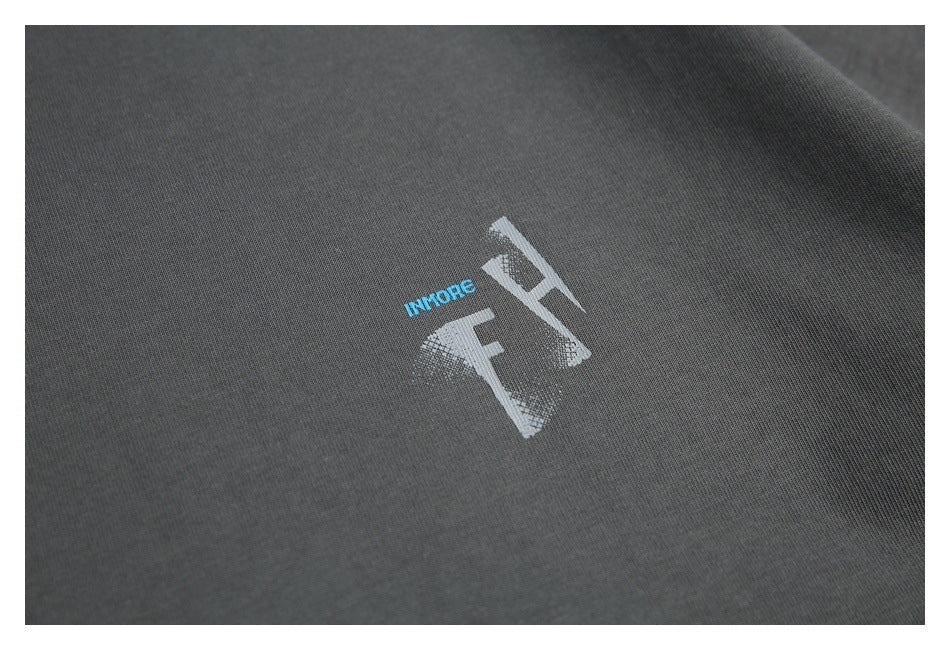 Close-up of the T-shirt's small distressed light-gray chest graphic and blue lettering on charcoal fabric.