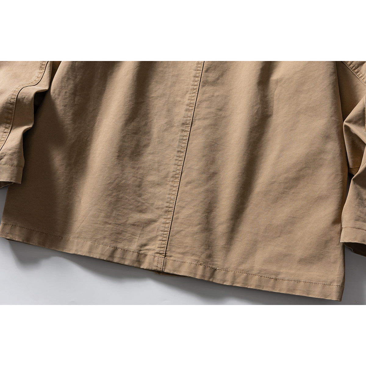 Close-up of the tan jacket's lower back, showing the center seam, hem, and sleeve edges.
