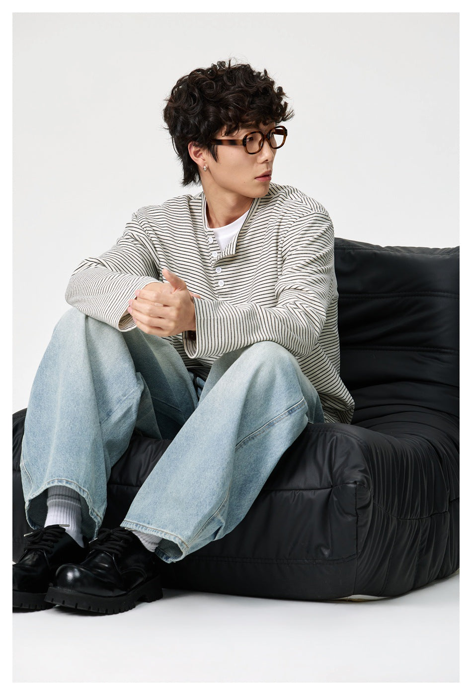 Seated model wearing an ivory thin-striped long-sleeve henley with light blue jeans.