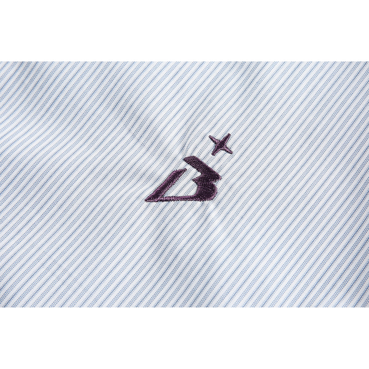 Close-up of a dark embroidered emblem on light blue and white striped shirt fabric.