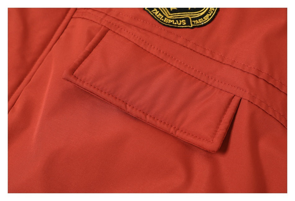 Close-up of a flap pocket and stitching on a rust-red coat, with part of an embroidered crest above.