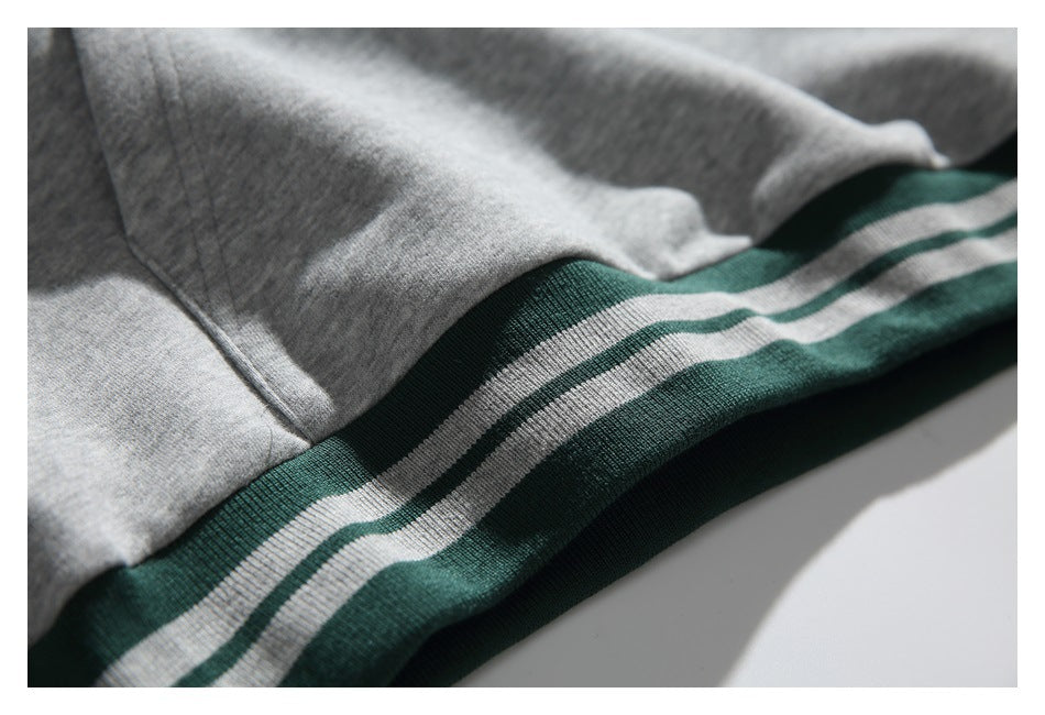 Close-up of gray sweatshirt fabric, pocket stitching, and dark green hem ribbing with light stripes.