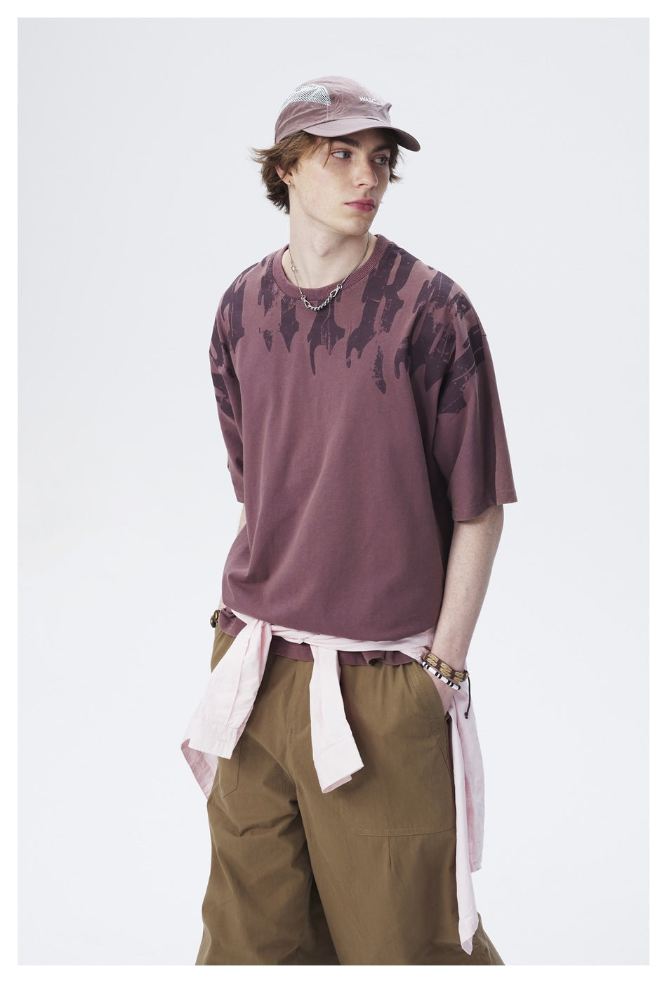 Three-quarter view of a model in a mauve oversized T-shirt with dark abstract shoulder graphics and olive cargo pants.