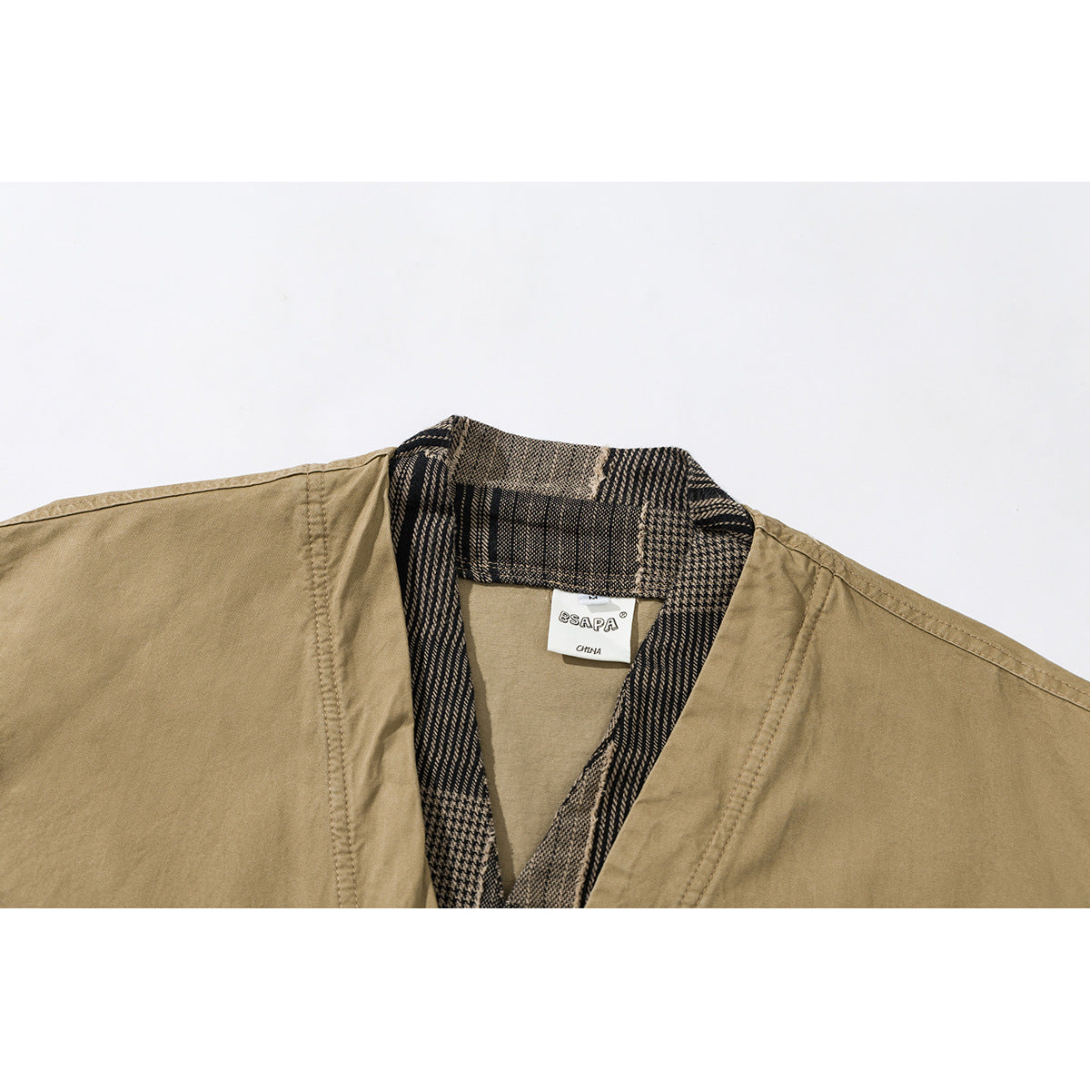 Close-up of a khaki jacket collar with dark plaid trim and a sewn neck label.